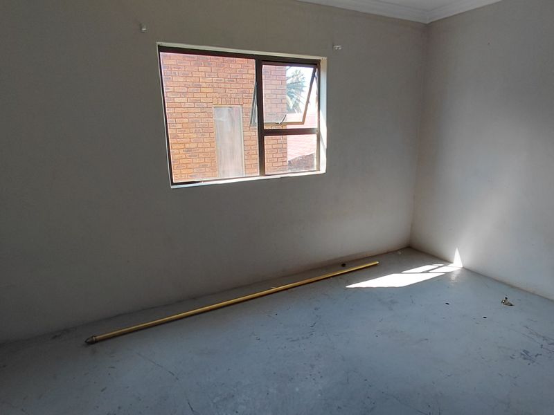 An empty bedroom featuring plain walls, a single aluminium window, and unfinished flooring, offering a blank canvas for renovation or interior design.