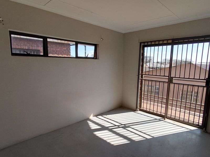 An empty bedroom featuring a sliding door with security gate and a horizontal window, providing natural light and access to an outdoor area.