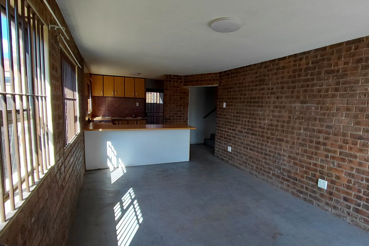 Open plan living area featuring exposed brick walls, concrete flooring, and a functional kitchen with a breakfast bar.