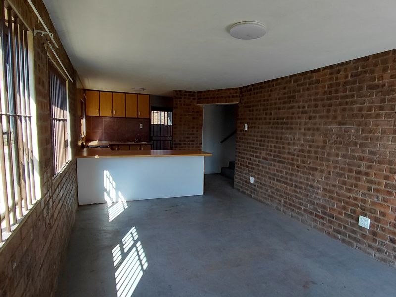 Open plan living area featuring exposed brick walls, concrete flooring, and a functional kitchen with a breakfast bar.