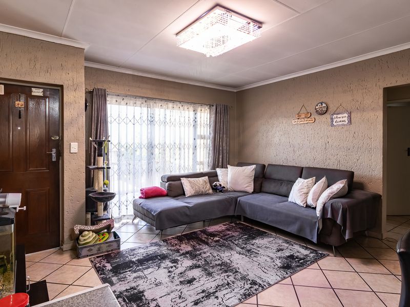 A comfortable living room featuring tiled flooring, textured walls, and a sliding glass door with a security gate, providing access to the exterior.