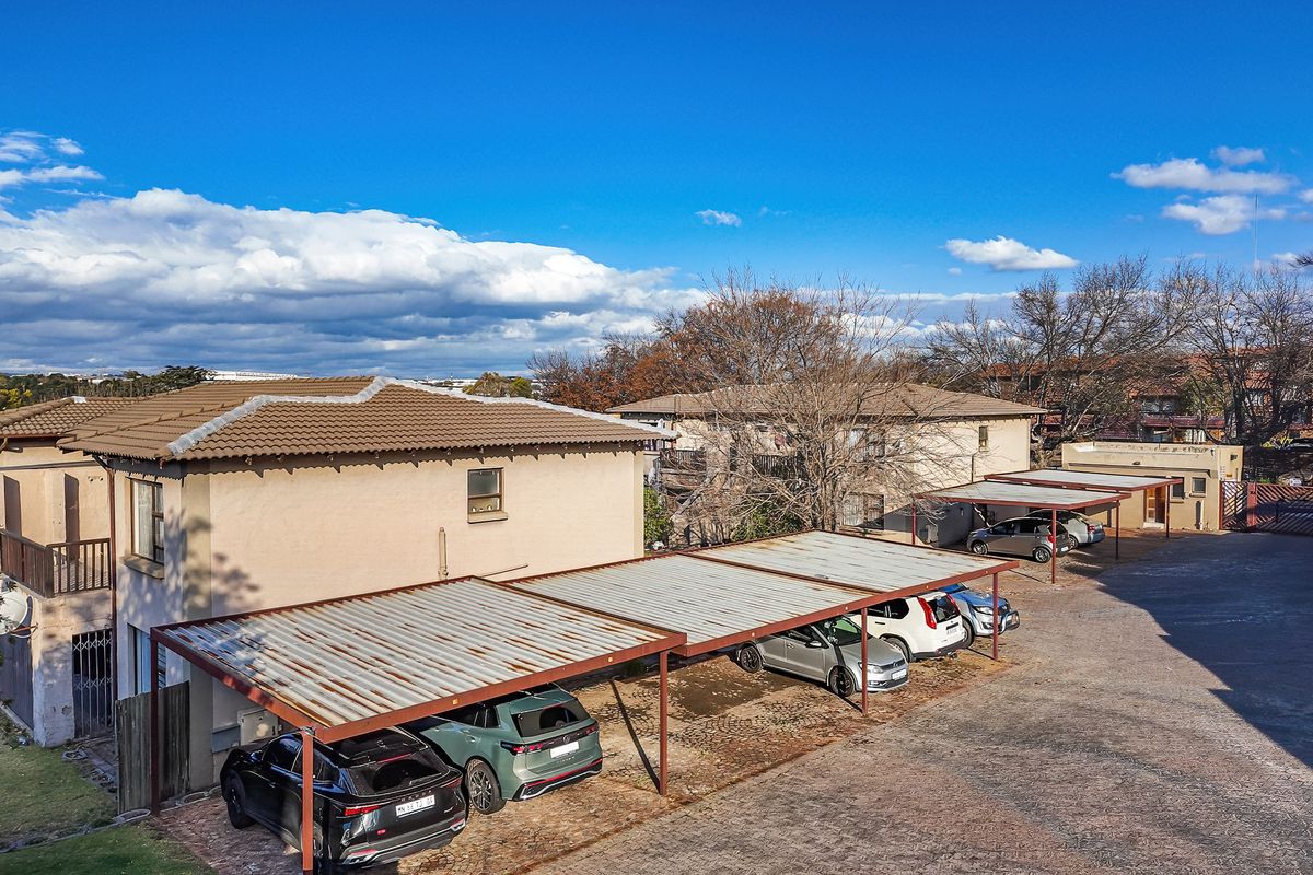 Aerial view of the townhouse complex showing the rear facade, paved driveway, and multiple covered carport parking bays.