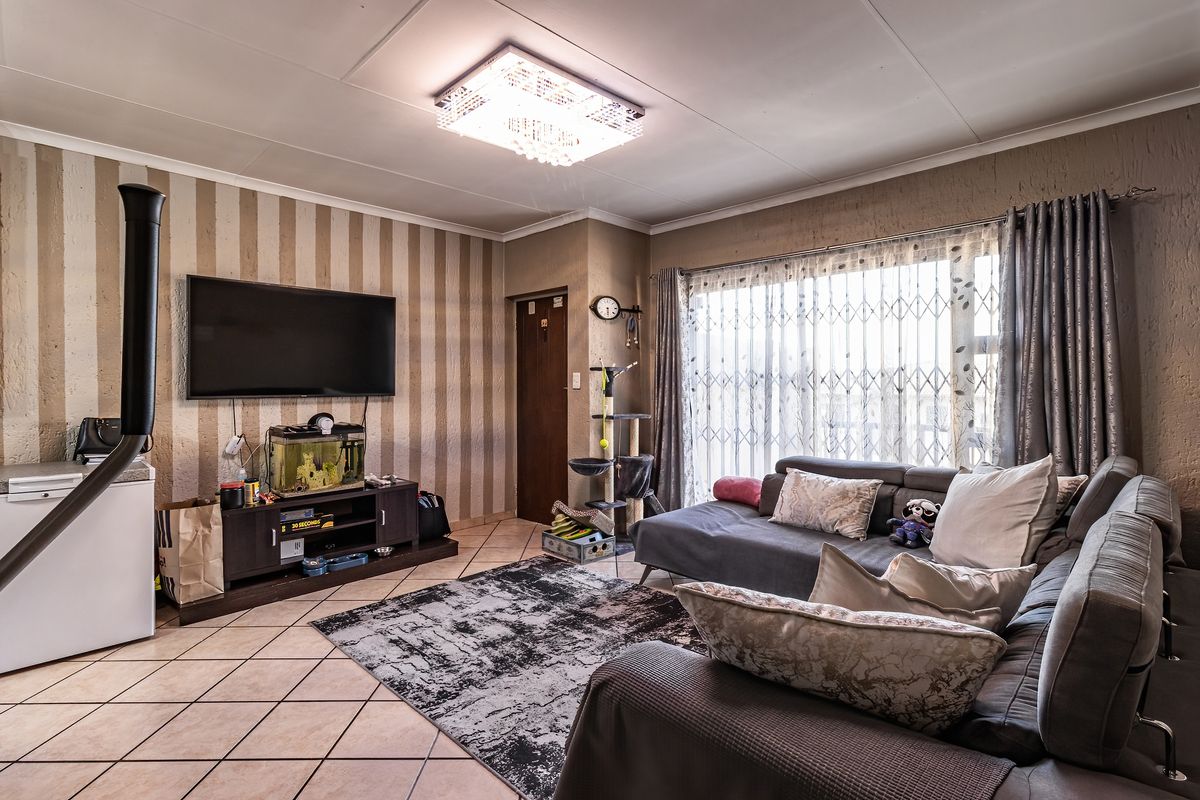 A living room featuring tiled flooring, a central ceiling light fixture, and a freestanding fireplace, with access to a patio through a security gate.