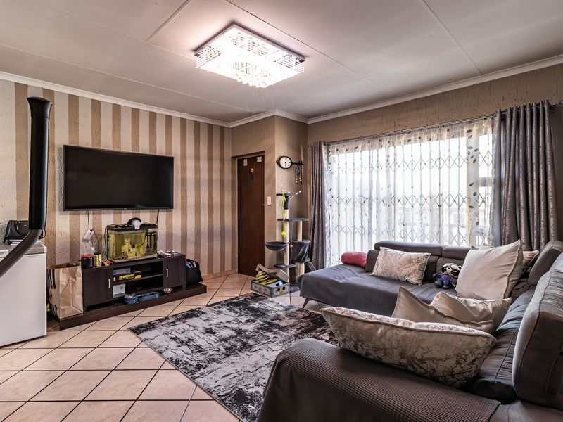 A living room featuring tiled flooring, a central ceiling light fixture, and a freestanding fireplace, with access to a patio through a security gate.