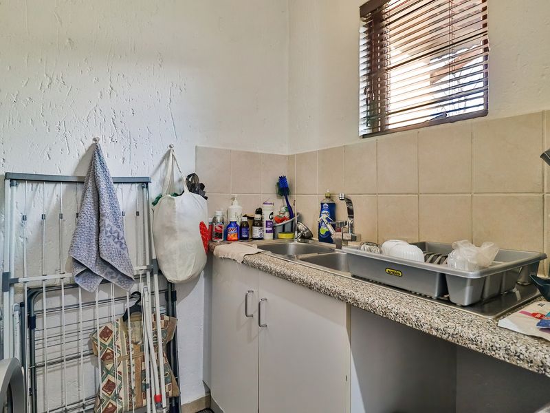 A functional laundry area featuring a stainless steel double sink, tiled backsplash, laminate countertop, and built-in cabinetry with a window for natural light.