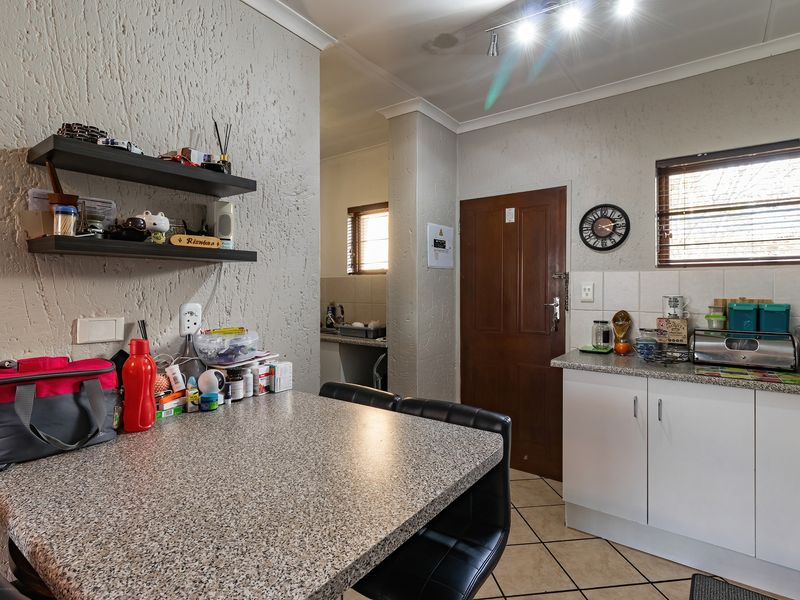 A functional kitchen featuring laminate countertops, built-in cabinetry, and tiled flooring, with an adjacent scullery area visible through the doorway.