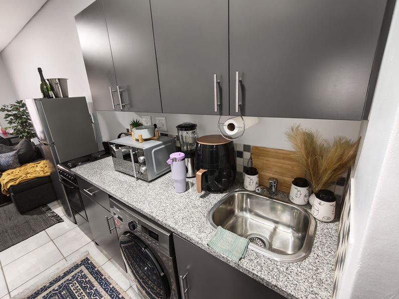 Modern kitchen featuring grey cabinetry, granite countertops, a stainless steel sink, and integrated appliances including a washing machine and oven.