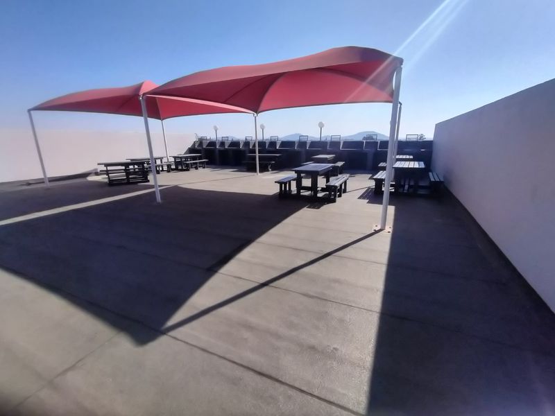 Spacious rooftop terrace featuring multiple built-in braai stations and large red shade sails, providing an ideal outdoor entertainment area.