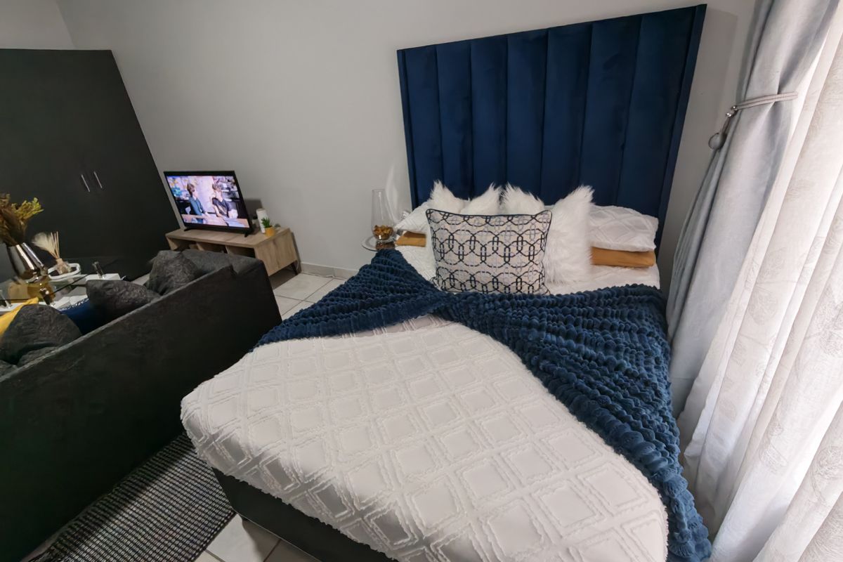 A well-maintained bedroom featuring tiled flooring and a prominent blue upholstered headboard, creating a comfortable and inviting sleeping space.