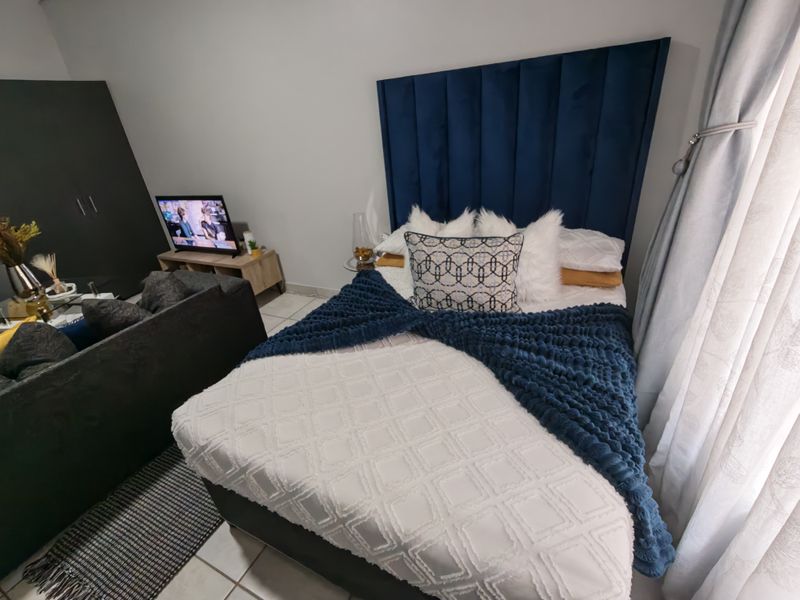 A well-maintained bedroom featuring tiled flooring and a prominent blue upholstered headboard, creating a comfortable and inviting sleeping space.