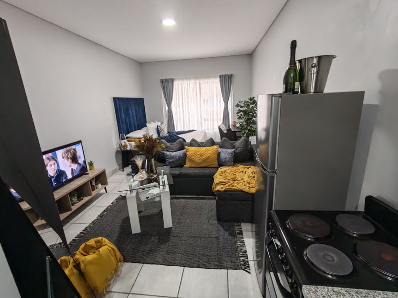 An open-plan studio apartment featuring a combined living and sleeping area with tiled flooring and a compact kitchen corner.