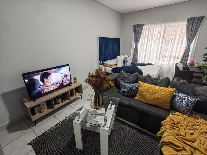 An open-plan living and bedroom area featuring tiled flooring and large windows with curtains, creating a functional and combined living space.