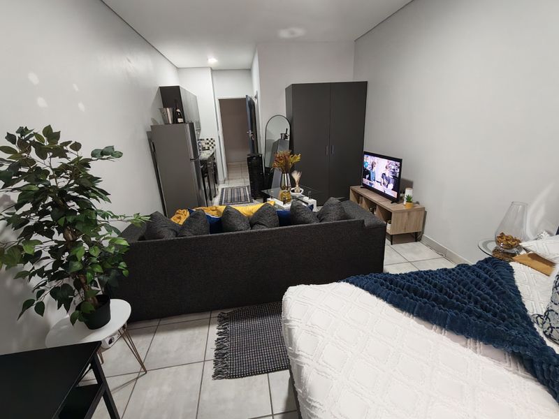 An open-plan studio apartment layout featuring tiled flooring, recessed lighting, and a compact kitchen area, offering a functional living and sleeping space.