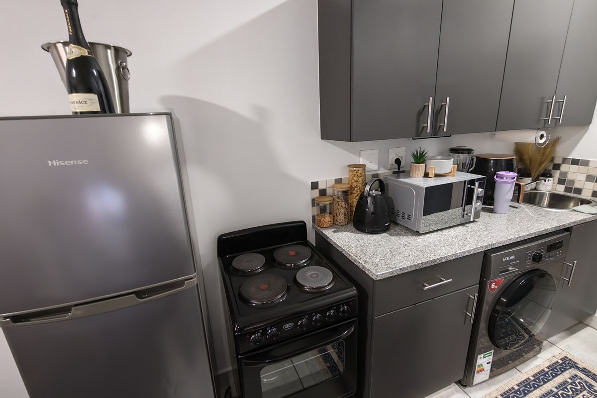 Modern kitchen featuring dark grey cabinetry, granite countertops, a tiled backsplash, and integrated space for a washing machine and electric stove.