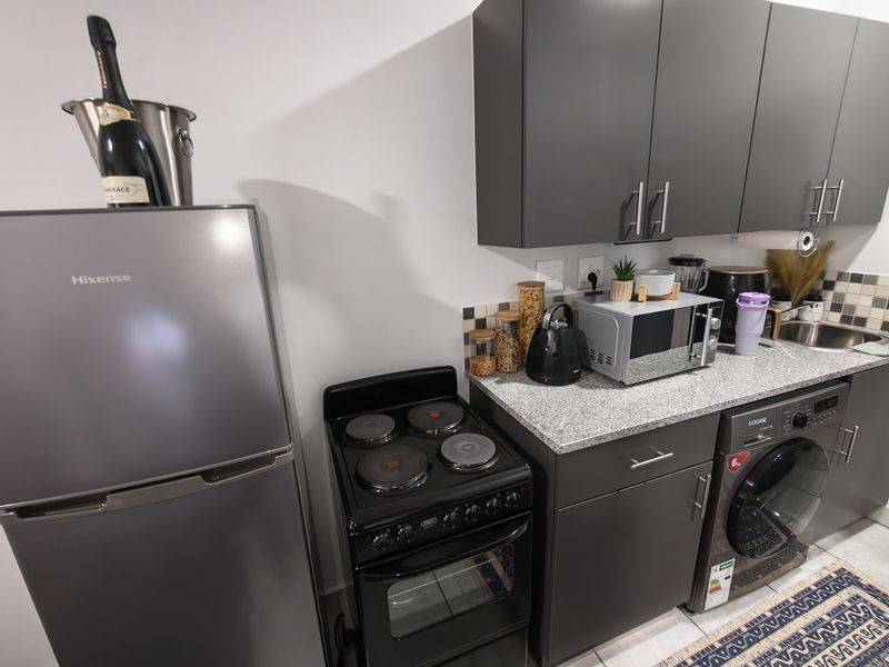 Modern kitchen featuring dark grey cabinetry, granite countertops, a tiled backsplash, and integrated space for a washing machine and electric stove.