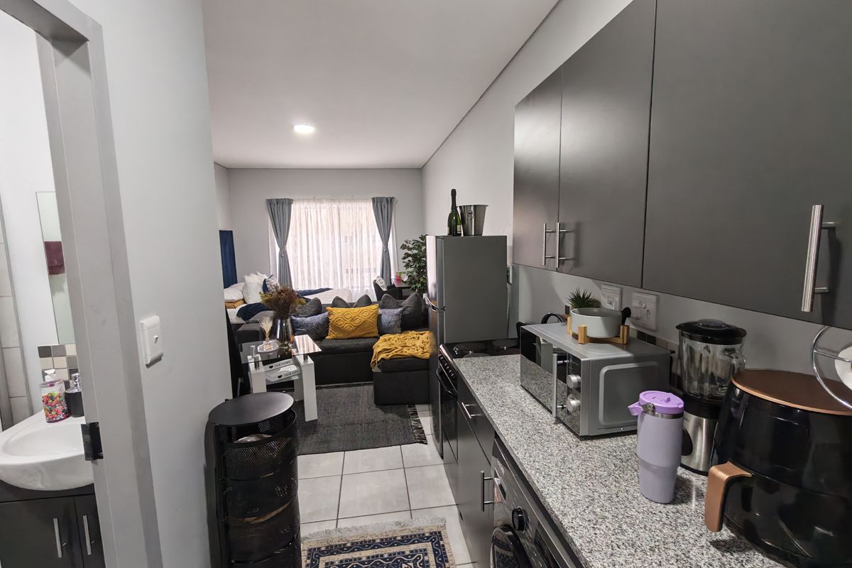 Open-plan apartment layout featuring a modern kitchen with granite countertops and cabinetry, flowing into a comfortable living area with tiled flooring throughout.