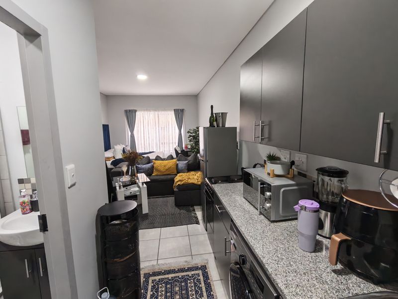 Open-plan apartment layout featuring a modern kitchen with granite countertops and cabinetry, flowing into a comfortable living area with tiled flooring throughout.