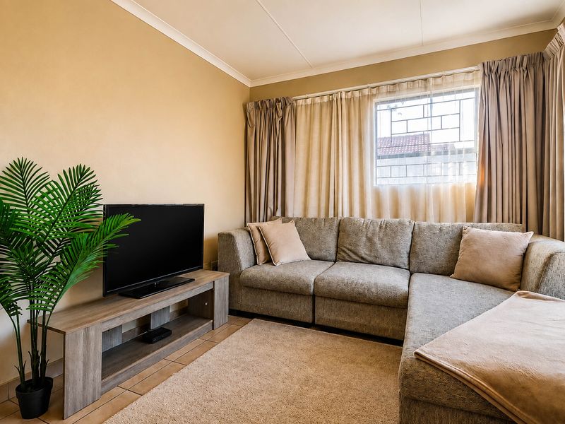 A comfortable living room featuring tiled flooring, neutral wall tones, and a window fitted with security bars.