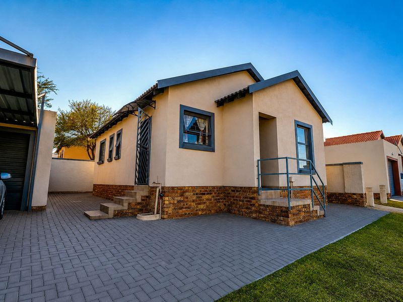 Front view of a well-maintained house featuring a paved driveway, face brick base, and secure metal entrance railings.