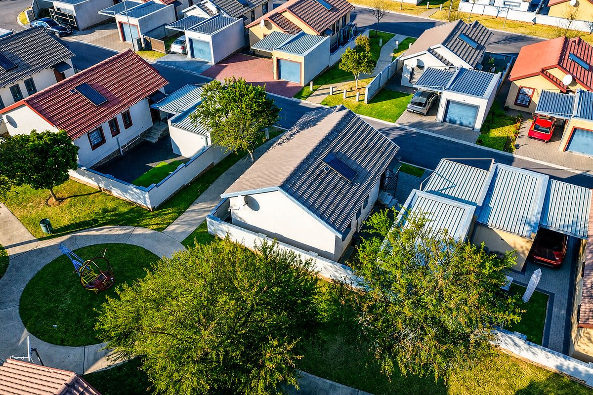 An aerial view of a residential estate showing multiple detached houses with tiled roofs, paved driveways, and private garden areas.
