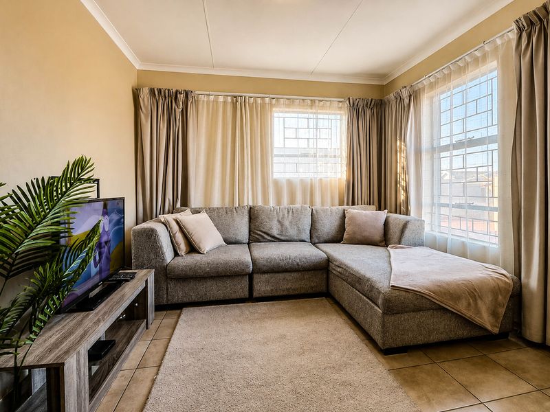 A comfortable living room featuring tiled flooring, large windows with security bars, and neutral wall tones, creating a bright and inviting space.
