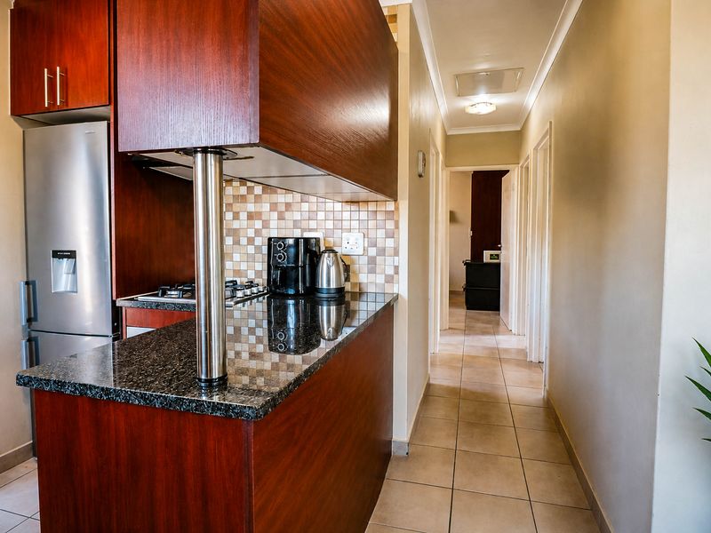 A functional kitchen featuring dark wood cabinetry, granite countertops, a mosaic tile backsplash, and a gas hob, leading into a tiled hallway.