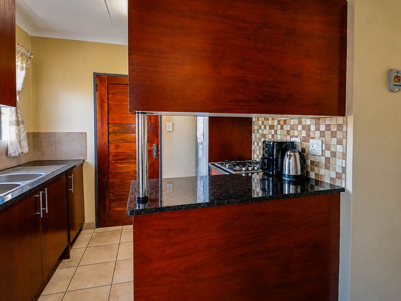 A functional kitchen featuring dark wood cabinetry, granite countertops, a gas hob, and a mosaic tile backsplash with tiled flooring.