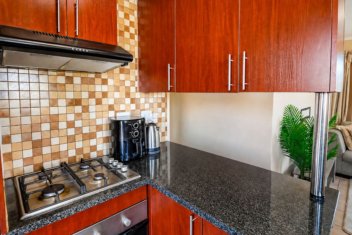 A functional kitchen featuring dark wood cabinetry, granite countertops, a gas hob, built-in oven, and a decorative mosaic tile backsplash.