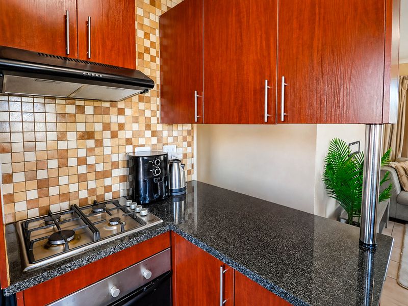 A functional kitchen featuring dark wood cabinetry, granite countertops, a gas hob, built-in oven, and a decorative mosaic tile backsplash.