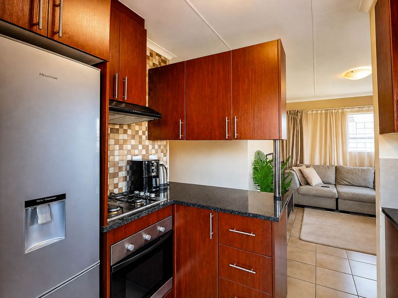 Open-plan kitchen featuring dark wood cabinetry, granite countertops, gas hob, and built-in oven, seamlessly flowing into the adjacent living area.