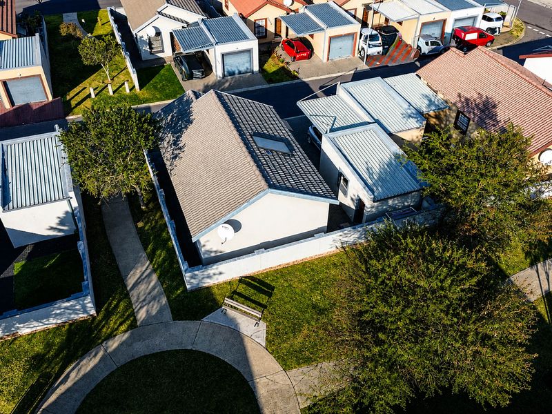 Aerial view of a residential property featuring a tiled roof with a skylight, surrounded by a boundary wall and landscaped garden areas.
