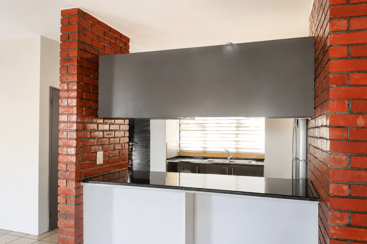 A clean kitchen featuring a breakfast bar with granite countertops, exposed brick architectural elements, and functional cabinetry with a stainless steel sink.