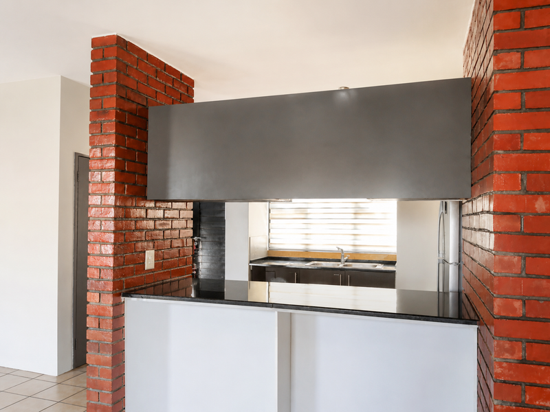 A clean kitchen featuring a breakfast bar with granite countertops, exposed brick architectural elements, and functional cabinetry with a stainless steel sink.