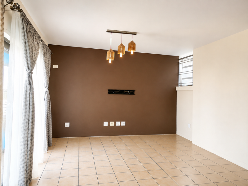 A bright, empty living room featuring neutral tiled flooring, a dark accent wall with television mounting hardware, and modern pendant lighting.