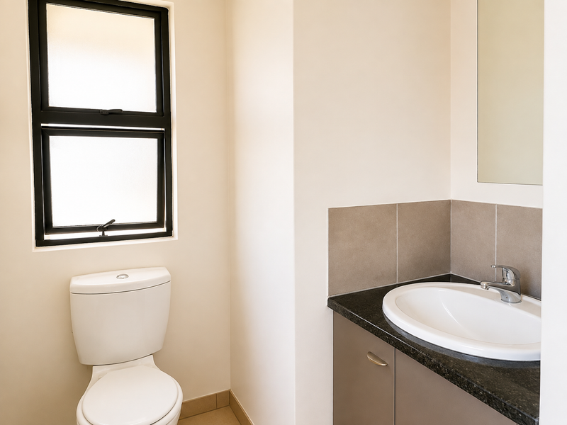 A clean and modern bathroom featuring a vanity with granite countertop, drop-in sink, wall mirror, and a toilet.