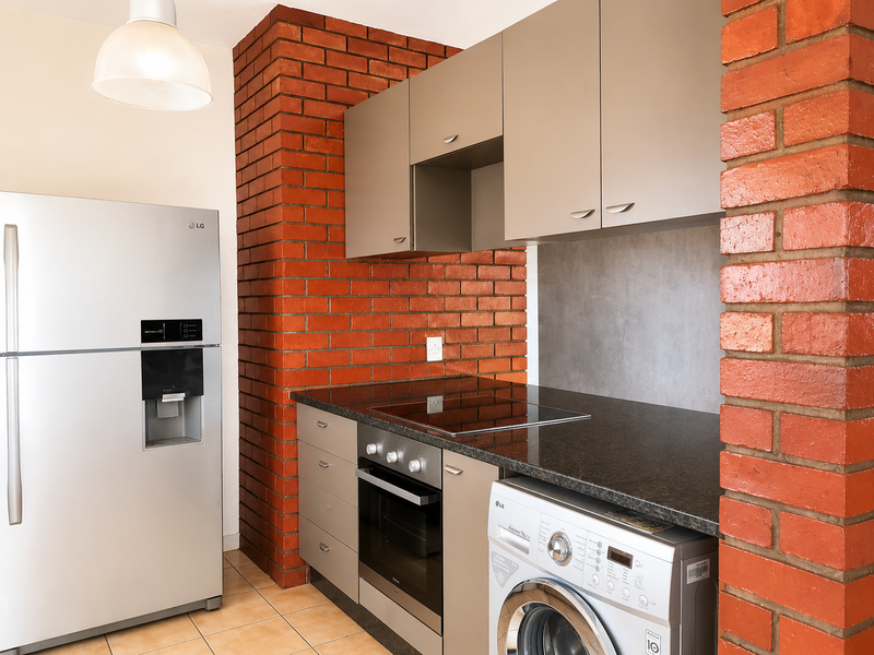 A modern kitchen featuring sleek cabinetry, granite countertops, an integrated electric hob and oven, and a striking exposed brick feature wall.