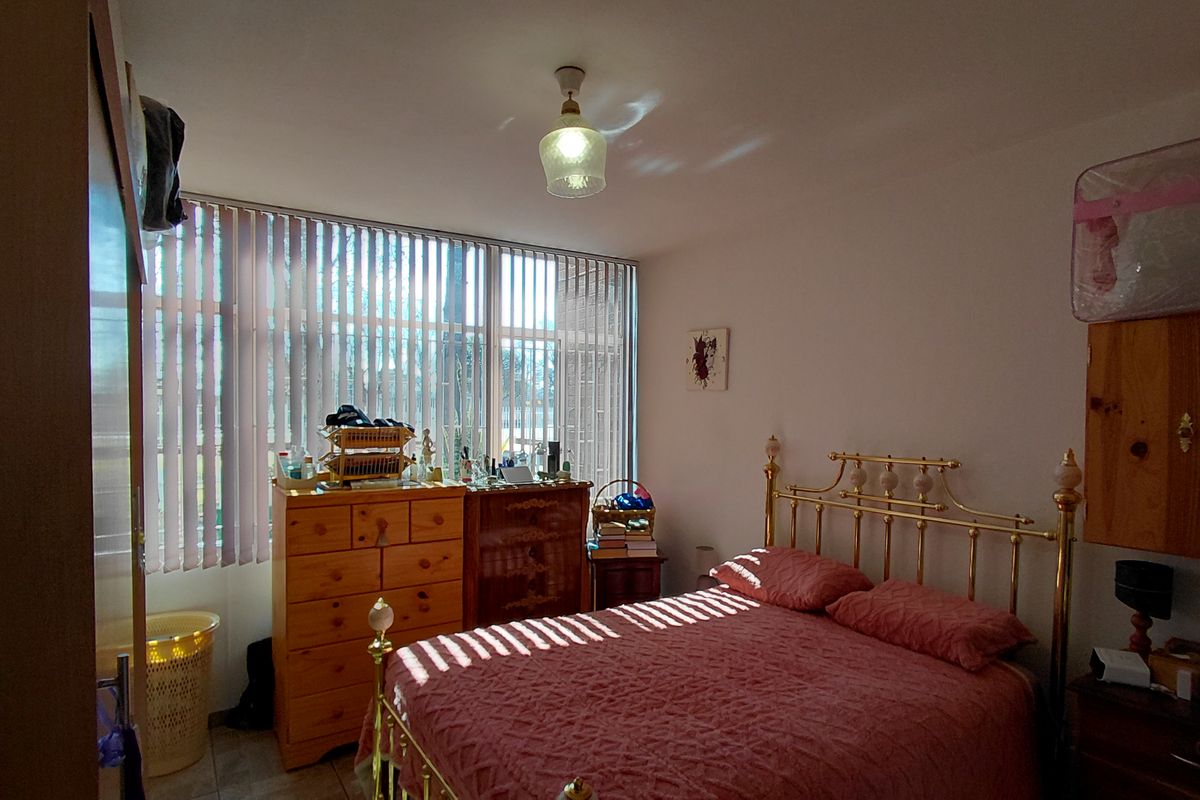 A standard bedroom featuring a large window with vertical blinds and neutral wall finishes, offering a functional space with natural light.
