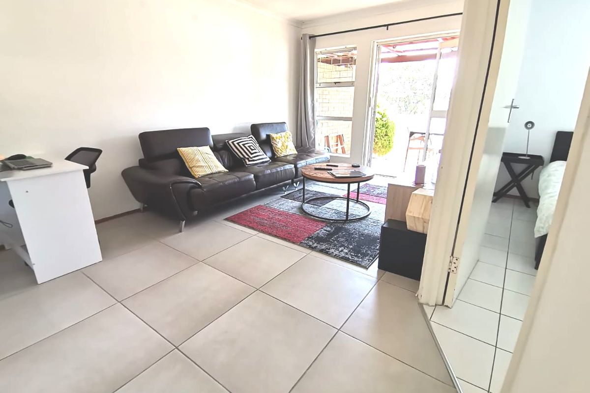 A bright living room featuring large format floor tiles and a sliding glass door providing direct access to the outdoor patio area.