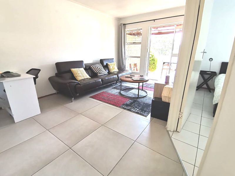 A bright living room featuring large format floor tiles and a sliding glass door providing direct access to the outdoor patio area.
