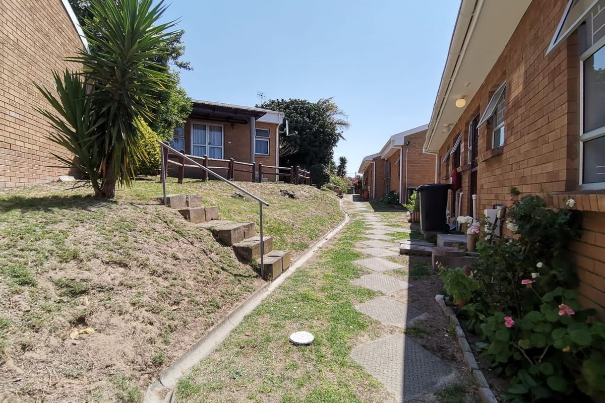 Exterior view of the townhouse complex featuring a brick facade, paved walkway, and landscaped garden area with concrete steps and metal handrail.