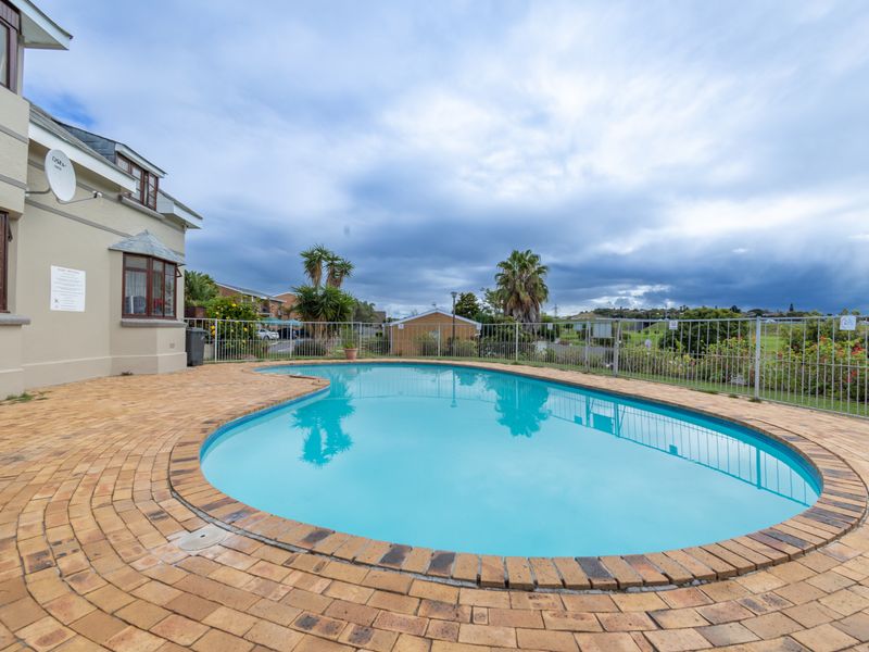 A well-maintained outdoor swimming pool area featuring brick paving and secure metal perimeter fencing, set against the townhouse exterior.