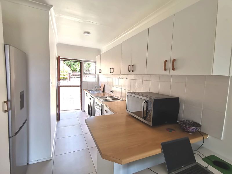 Functional kitchen featuring white cabinetry, tiled backsplash, electric hob, built-in oven, and a breakfast counter, with direct access to the exterior.