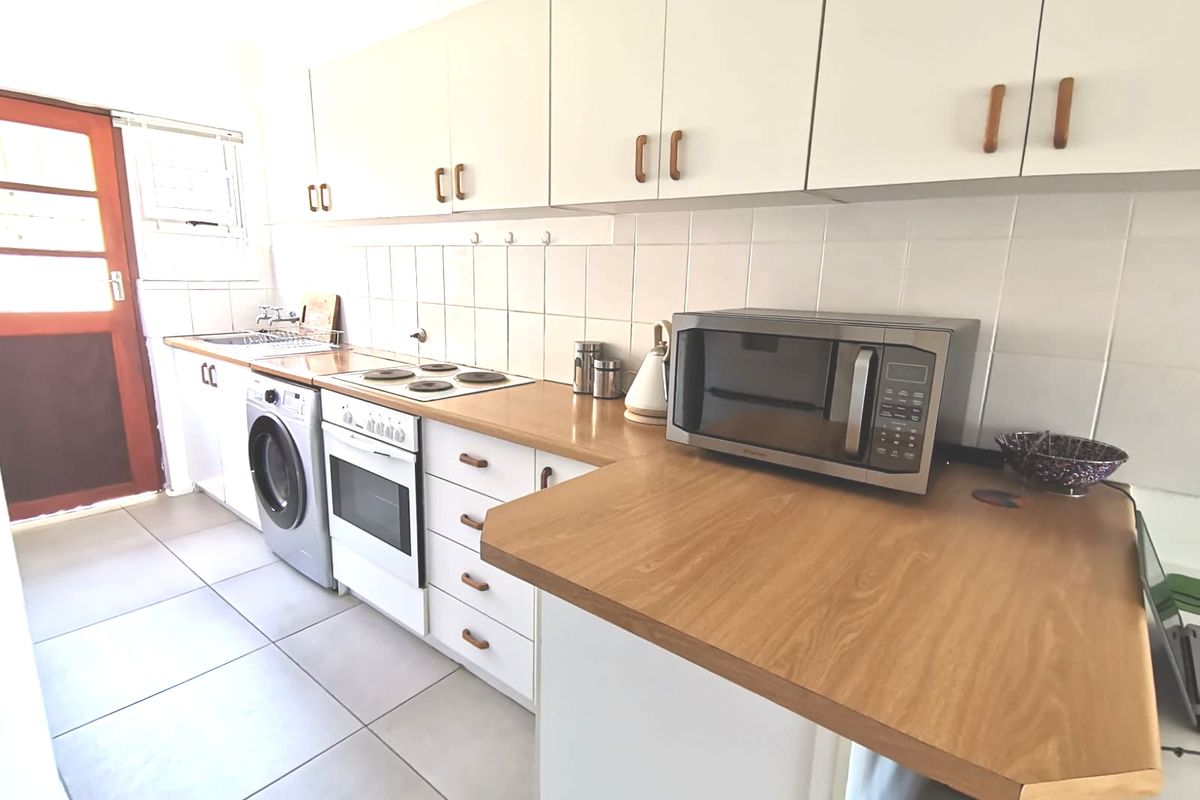 Functional kitchen featuring white cabinetry, laminate countertops, tiled backsplash, and integrated electric cooking appliances with direct access to the exterior.