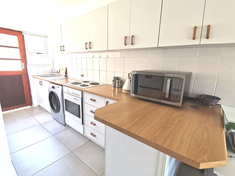 Functional kitchen featuring white cabinetry, laminate countertops, tiled backsplash, and integrated electric cooking appliances with direct access to the exterior.