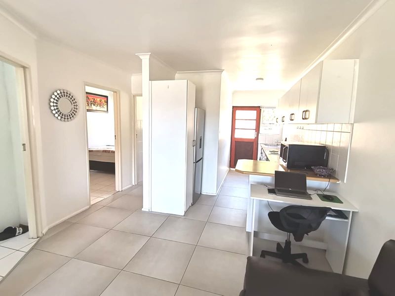 Open plan kitchen and living area featuring tiled flooring, neutral walls, and functional built-in cabinetry with direct access to adjacent rooms.