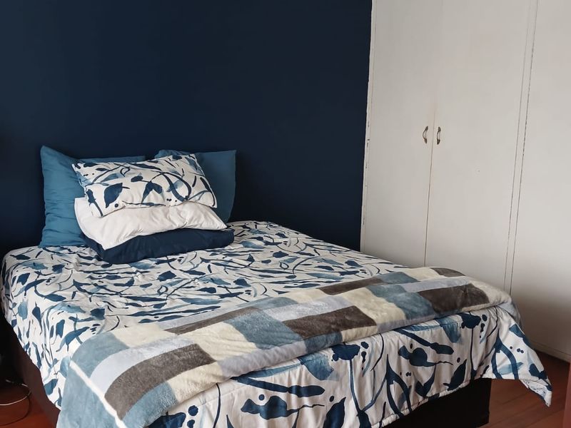 A well-maintained bedroom featuring dark blue accent wall, built-in white cabinetry, and polished hardwood flooring with an integrated air conditioning unit.