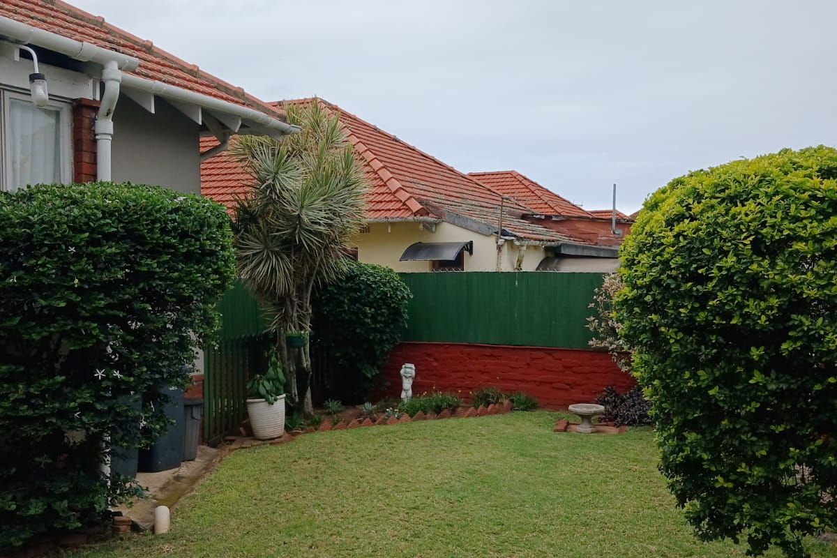 A view of the rear garden featuring a lawn area, established shrubs, and a boundary fence with a brick retaining wall.