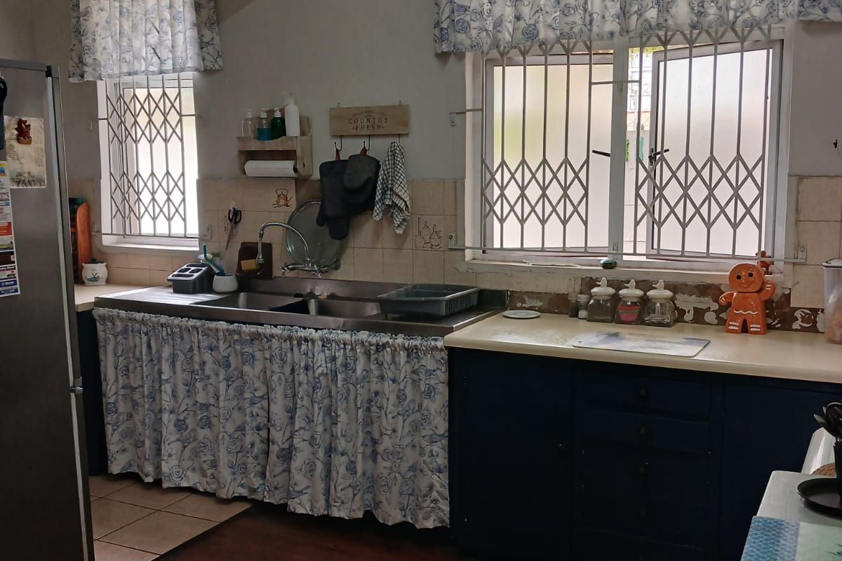 A dated kitchen featuring timber flooring, a double stainless steel sink, and built-in cabinetry with curtain-style lower cabinet covers.