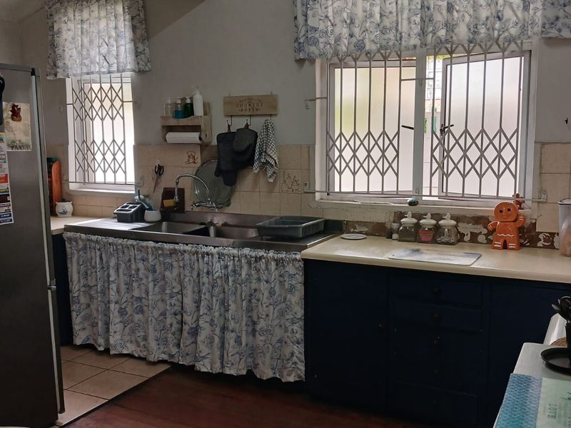 A dated kitchen featuring timber flooring, a double stainless steel sink, and built-in cabinetry with curtain-style lower cabinet covers.