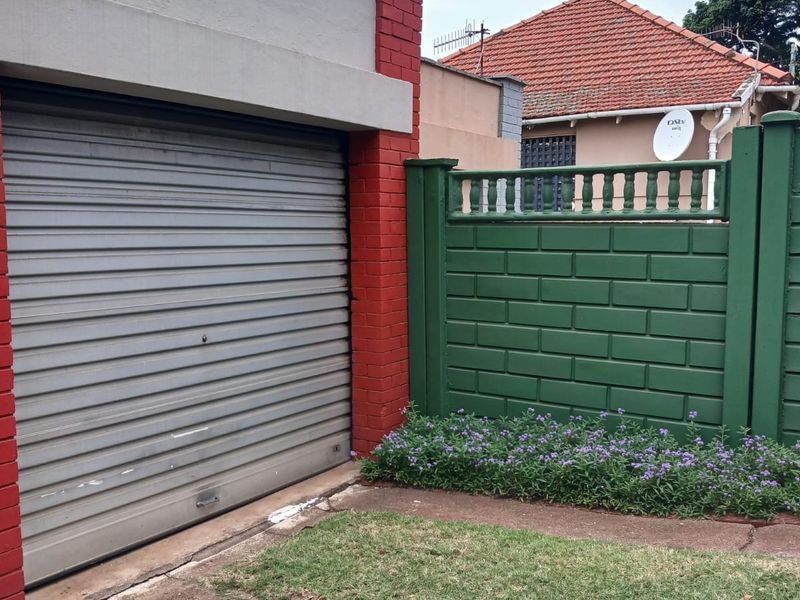 Front view of the property featuring a roller shutter garage door, concrete driveway, and a painted brick boundary wall.